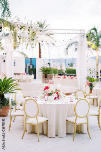 Covered festive tables with bright bouquets of flowers stand near a decorated illuminated stage © Nadtochiy