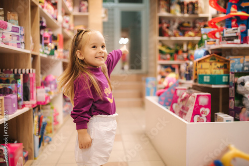 Adorable little girl shopping for toys. Cute female in toy store. Happy young girl selecting toy
