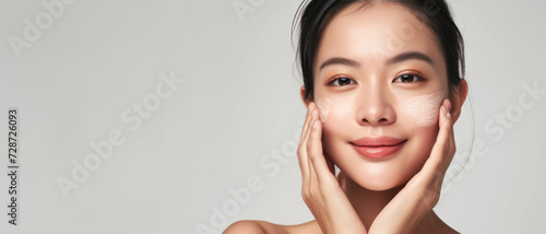 The epitome of skincare routine, a young Asian woman applies facial cream, her skin radiant with a healthy glow