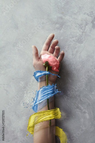 A hand with a tender pink rose, splashed in Ukrainian flag colors