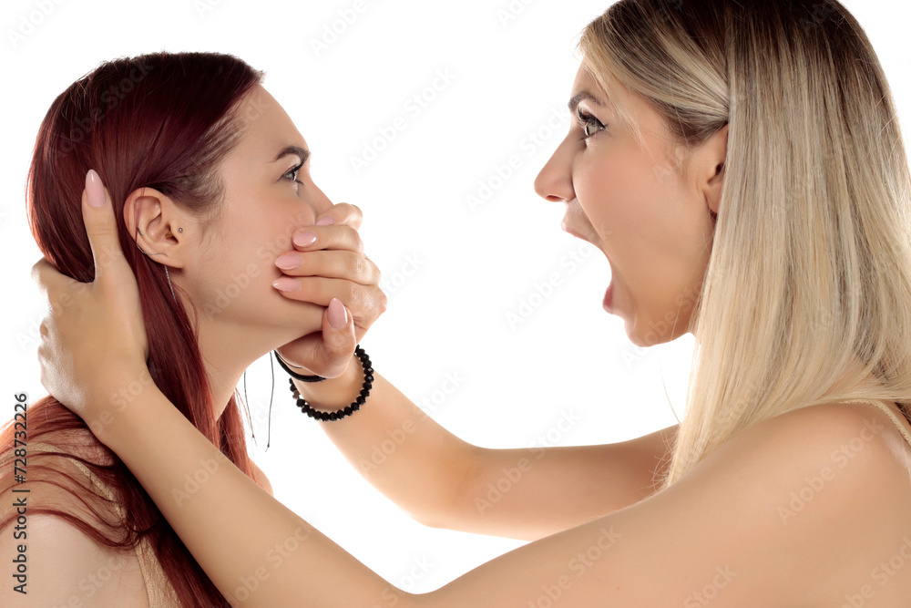 Angry young woman covering yelling girlfriend mouth using hand as arguing couple relationship concept isolated on white background Angry young woman covering yelling girlfriend mouth using hand as arguing couple relationship concept isolated on white background
