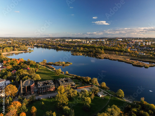 Aerial view of Bagry lake and autumn forest in Poland. Amazing panoramic landscape with waters of spectacular Bagry lagoon and road along beach, houses of town and scenic tops of trees under blue sky