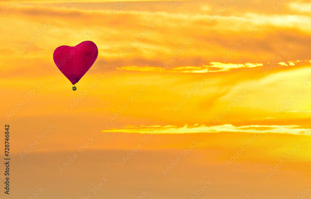 Obraz premium Red heart shaped hot air balloon flying over sunset sky 