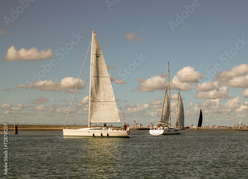 sailboats are sailing out the harbour of Breskens in a row towards the north sea in summer and a blue sky with clouds