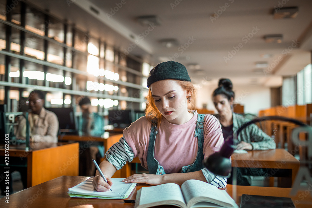 Focused female student studying and writing notes in college library Focused female student studying and writing notes in college library