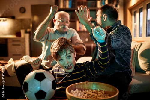 Young boy watching a football match with his father and grandfather in the living room