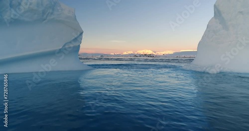 Melted hole in Antarctic iceberg drifting blue ocean water. Environment ecological issue of global warming. Polar climate change at sunset winter day. Low angle drone shot between two glaciers