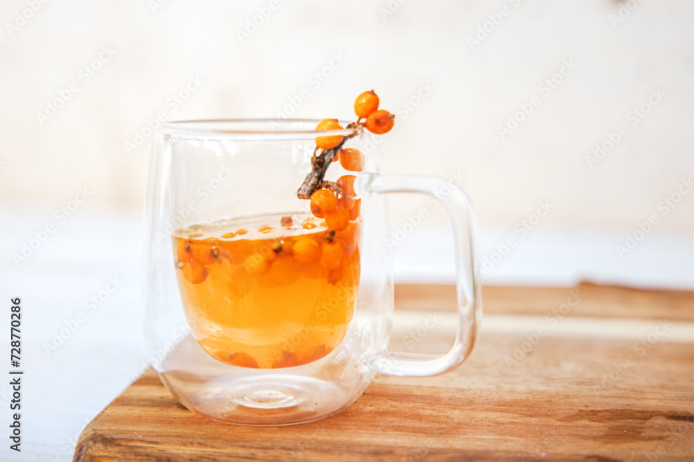 Cup with fragrant vitamin tea from sea buckthorn on a wooden table. Fresh sea buckthorn berries on a branch are ready for the preparation of a healing drink Cup with fragrant vitamin tea from sea buckthorn on a wooden table. Fresh sea buckthorn berries on a branch are ready for the preparation of a healing drink