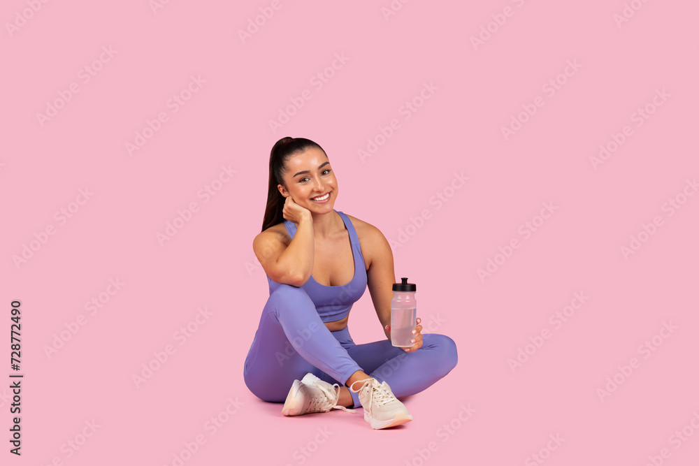 Young woman in sportswear with water bottle, smiling on pink background Young woman in sportswear with water bottle, smiling on pink background