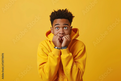 Nervous African American teenage boy and biting nails in studio with oops reaction to gossip on yellow background. Mistake, sorry, drama or secret with regret, shame or awkward photo