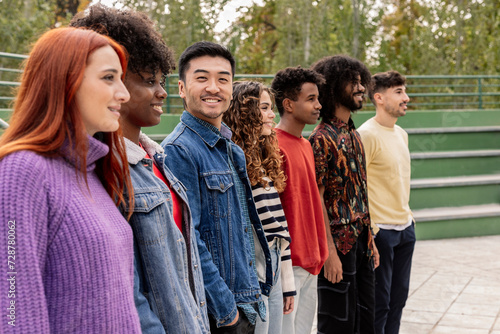 group of multiracial friends placed in a line and one of them looks at camera smiling
