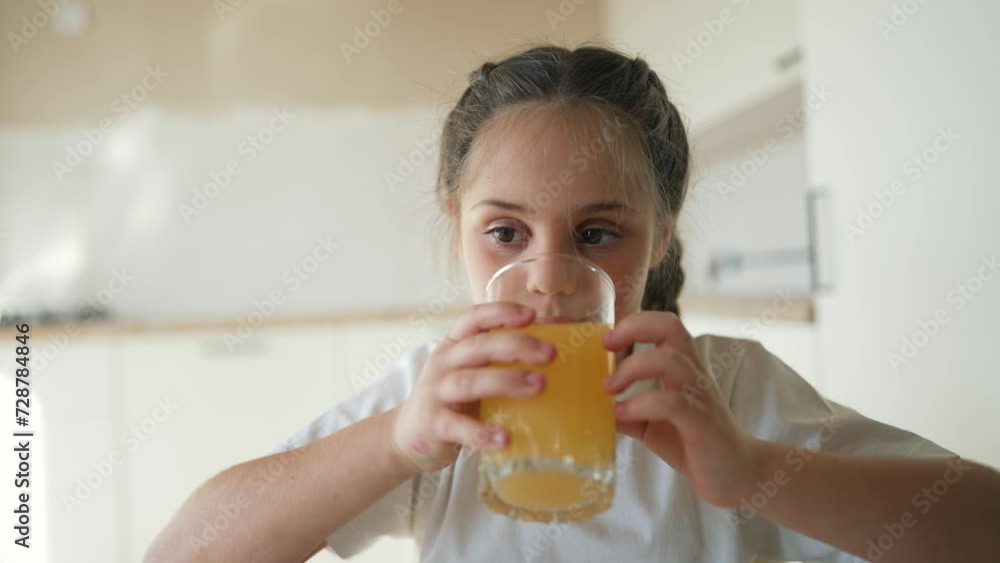 Little cute girl drinks fresh fruit juice. Happy child drinking orange drink. Healthy breakfast for a child. Girl drinks orange juice at the table in the kitchen. Healthy drink for a healthy lifestyle Little cute girl drinks fresh fruit juice. Happy child drinking orange drink. Healthy breakfast for a child. Girl drinks orange juice at the table in the kitchen. Healthy drink for a healthy lifestyle