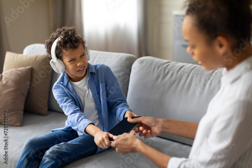 Canvas Print Mother taking tablet from reluctant child with headphones