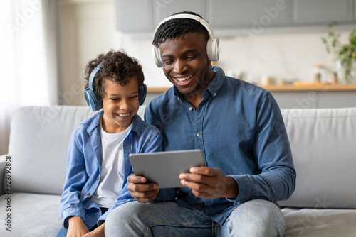 Joyful black father and son using tablet with headphones