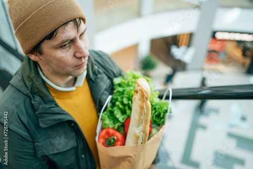 Man holds paper bag filled with various food items in his hand in mall photo