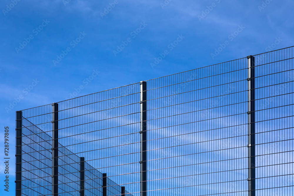 Modern high fencing with metal fence against blue sky. Diagonal, copy space