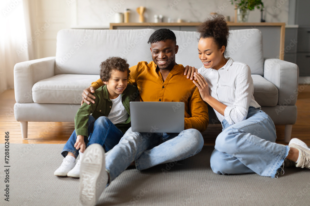 Black family with laptop enjoying time together on floor at home Black family with laptop enjoying time together on floor at home