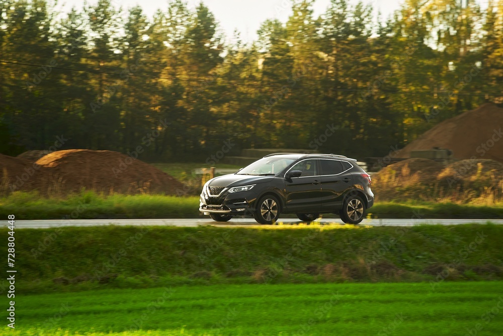 A modern and luxurious SUV car travels on an asphalt road with a breathtaking landscape of a golden sunset sky.