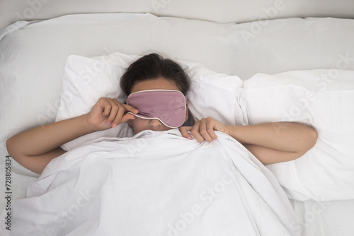 pretty woman wakes up lifting sleep mask in bedroom of apartment waking up after resting  photo