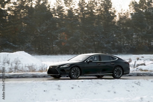 Modern car during snow storm go on the highway. Side view of the car in winter on the road. Necessity of winter tires during slippery and cold weather conditions. Below zero. © AlexGo