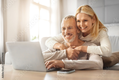 Loving european retired couple planning vacation together, using laptop photo