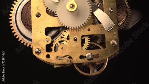 clockwork mechanism of an old ALARM CLOCK  going off disassembled with golden cogwheels running on silver steel closeup gear movement working close-up front view detail antique watch isolated on black photo
