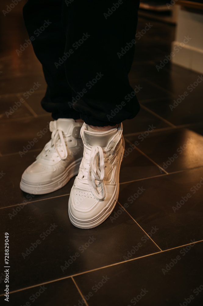 The image is of a persons feet wearing white shoes on a tile floor 6073. The image is of a persons feet wearing white shoes on a tile floor 6073.