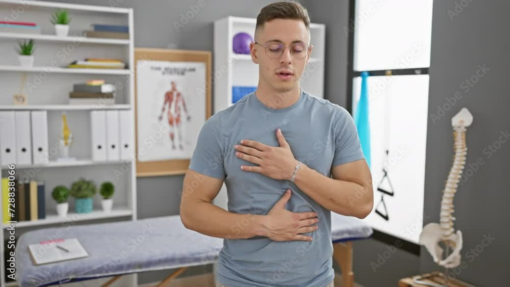 Young hispanic man practicing deep breathing exercises in a clinic room with medical posters and a skeleton model. Young hispanic man practicing deep breathing exercises in a clinic room with medical posters and a skeleton model.