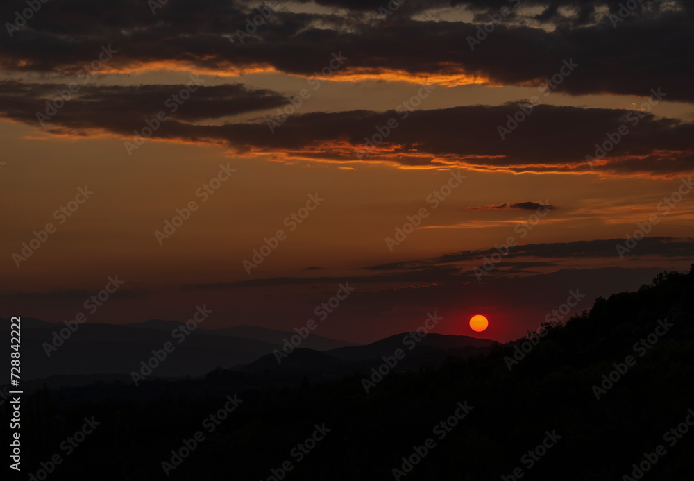 Beautiful sunset in the mountains. Sunset View from the Top of a Mountain. Sunset in strong orange tones in Serbia. The sun falls for horizon, a sunset. Shadows are condensed, beautiful clouds.