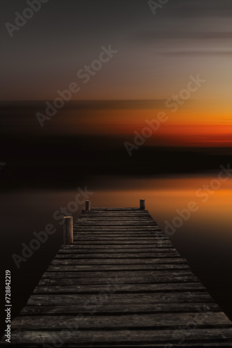 Abstract lake landscape at sunset with an old wooden boardwalk. Dock in lake with abstract blurred background in dark sunset evening