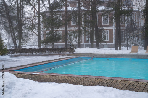 Outdoor hotel spa swimming pool with warm water without people. Winter wellness resort with hot open-air swimming pool with thermal water, foggy weather