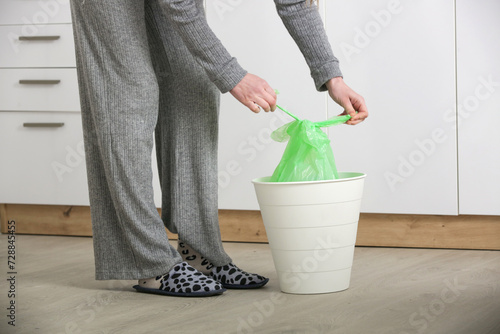 Housewife throwing away garbage, taking of plastic garbage bag from the trash bin in the apartment	

