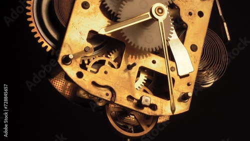 clockwork mechanism of an old ALARM CLOCK  disassembled with golden clockhands turning slowly on silver steel gear movement working closeup low angle shot detail antique watch isolated on black