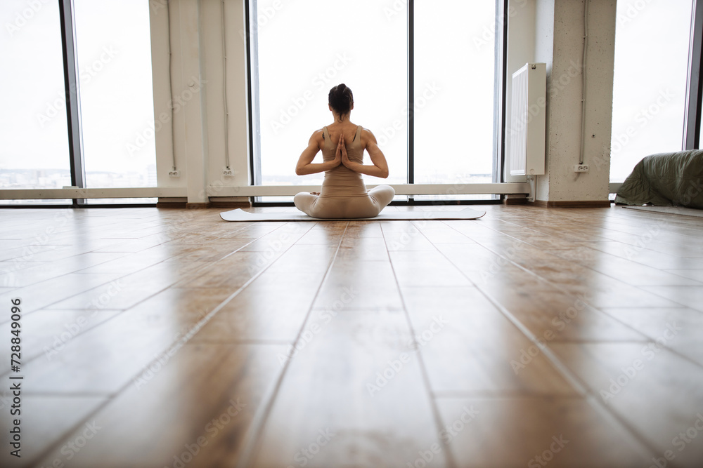 Middle aged women practicing yoga in Lotus pose or Padmasana with raised hands namaste behind the back. Meditation with yoga in in front of window in fitness studio in morning. Middle aged women practicing yoga in Lotus pose or Padmasana with raised hands namaste behind the back. Meditation with yoga in in front of window in fitness studio in morning.