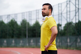 Confident man looking into distance and holding hands in waist at training at city sports stadium professional sportsman enjoying jogging on modern track