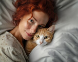 Smiling curly woman lies in bed with ginger cat. Close up portraits of pet and redhead woman. Tranquil home scene at bedroom. Dark key photography. 