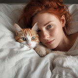 Smiling curly Irish woman lies in bed with ginger cat. Close up portraits of pet and redhead woman. Tranquil home scene at bedroom. Dark key photography.