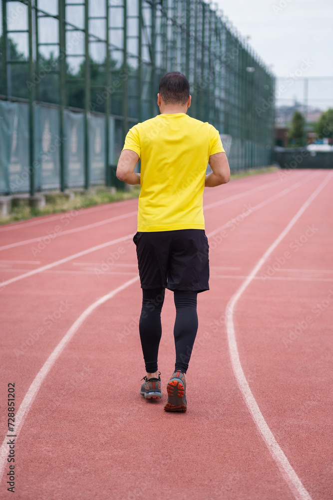 Active man in comfortable activewear jogs along the stadium track, healthy and active lifestyle backside view. 