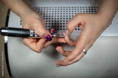 Female Nail technician using electric nail file to remove gel nail polish from her finger nails. DIY nails