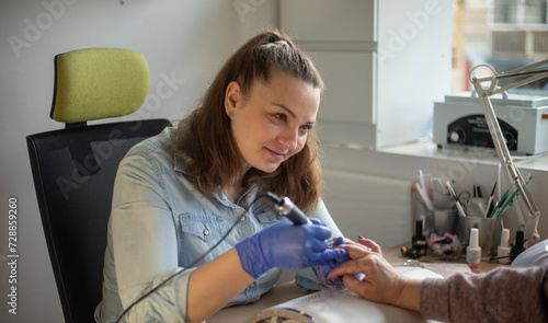 Female nail technician focused while doing her client's nail using electric nail file. 