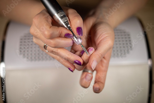 Female Nail technician using electric nail file to remove gel nail polish from her finger nails. DIY nails