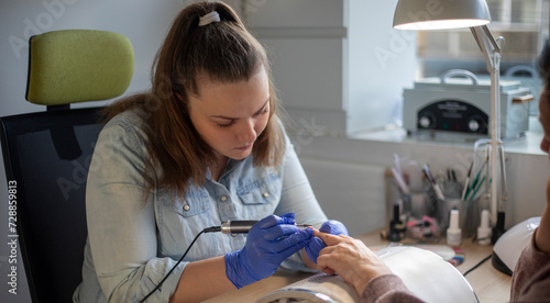 Female nail technician focused while doing her client's nail using electric nail file. 
