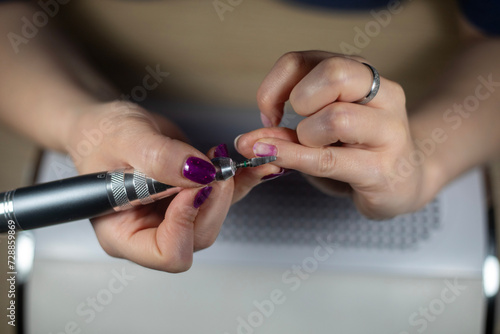 Female Nail technician using electric nail file to remove gel nail polish from her finger nails. DIY nails