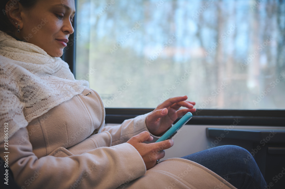 Close-up of a young woman commuter, passenger scrolling news feed on her smartphone, enjoying a comfortable trip