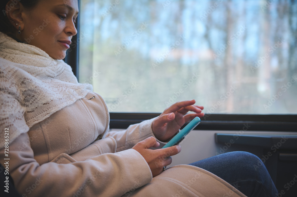 Close-up of a young woman commuter, passenger scrolling news feed on her smartphone, enjoying a comfortable trip Close-up of a young woman commuter, passenger scrolling news feed on her smartphone, enjoying a comfortable trip