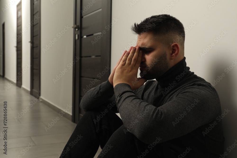 Sad man sitting on floor in hall. Space for text Sad man sitting on floor in hall. Space for text