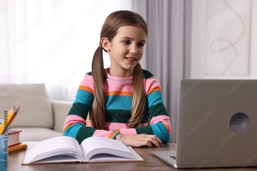 E-learning. Cute girl using laptop during online lesson at table indoors E-learning. Cute girl using laptop during online lesson at table indoors