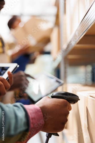 African american distribution warehouse worker arm scanning cardboard box code. Logistics manager cheking goods in stock using barcode scanner on freight parcels in storehouse photo