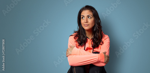 Mujer joven con expresión de estar pensando o dudando sentada frente a un fondo liso azul