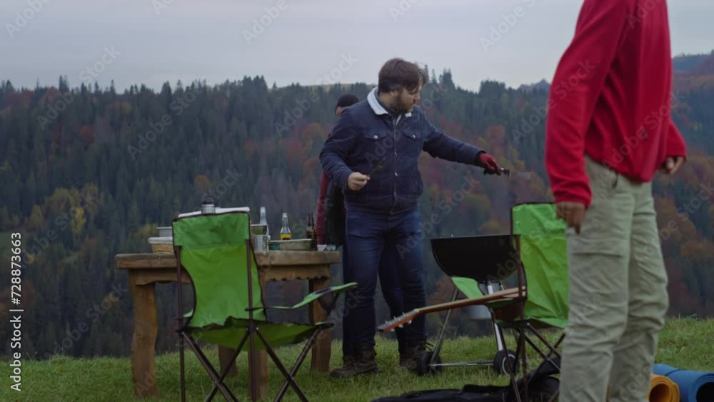 Two men together cook food on grill and dance on beautiful hill. Group of multi ethnic travelers stopped to rest after long expedition at mountains. Nature discovery and tourism concept. Slow motion. Two men together cook food on grill and dance on beautiful hill. Group of multi ethnic travelers stopped to rest after long expedition at mountains. Nature discovery and tourism concept. Slow motion.